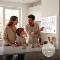 A family of three stands at a kitchen island in a bright modern kitchen, looking at and pointing at a large illuminated smart kitchen board mounted on the wall. A circular badge in the lower right highlights 2GB RAM and 32GB storage.
