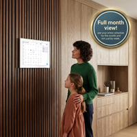 Woman and child looking at a digital calendar on a wall in a kitchen.