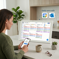 Woman using a digital assistant on a large screen with smartphone, mug, and plant in a home office setting.